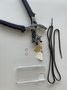DIY-Idee: Materialien für Handykette: Schnürsenkel, Handyhülle, Lochzange, kleine Metallringe, Quasten, Dekoration