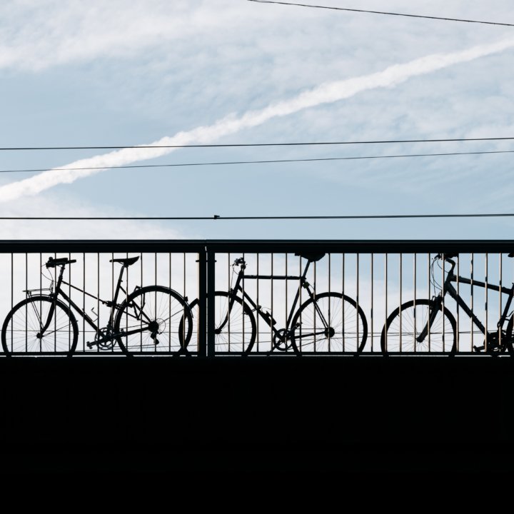 Silhouette d'un homme avec un sac à dos passant devant trois vélos enchaînés à une rambarde de pont.